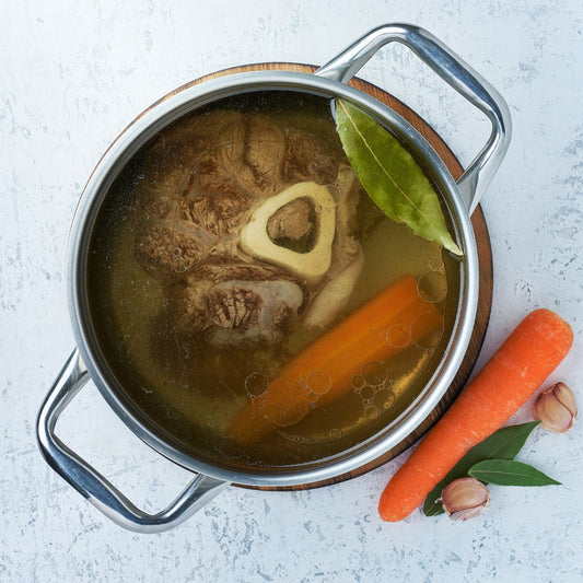 "Imagen de una olla de caldo de huesos casero, humeante y reconfortante. El caldo está preparado con huesos de calidad y una variedad de verduras frescas, creando un plato lleno de sabor y nutrientes. mejorar tu bienestar