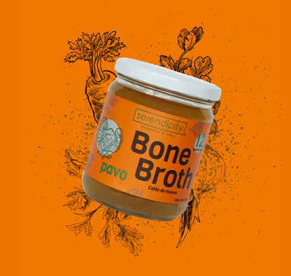Frasco de caldo de hueso de pavo de la marca 'serendipity' con una etiqueta blanca, flotando frente a un fondo naranja con ilustraciones de hierbas. La etiqueta muestra  el texto 'Bone Broth, cordero, Caldo de Huesos'